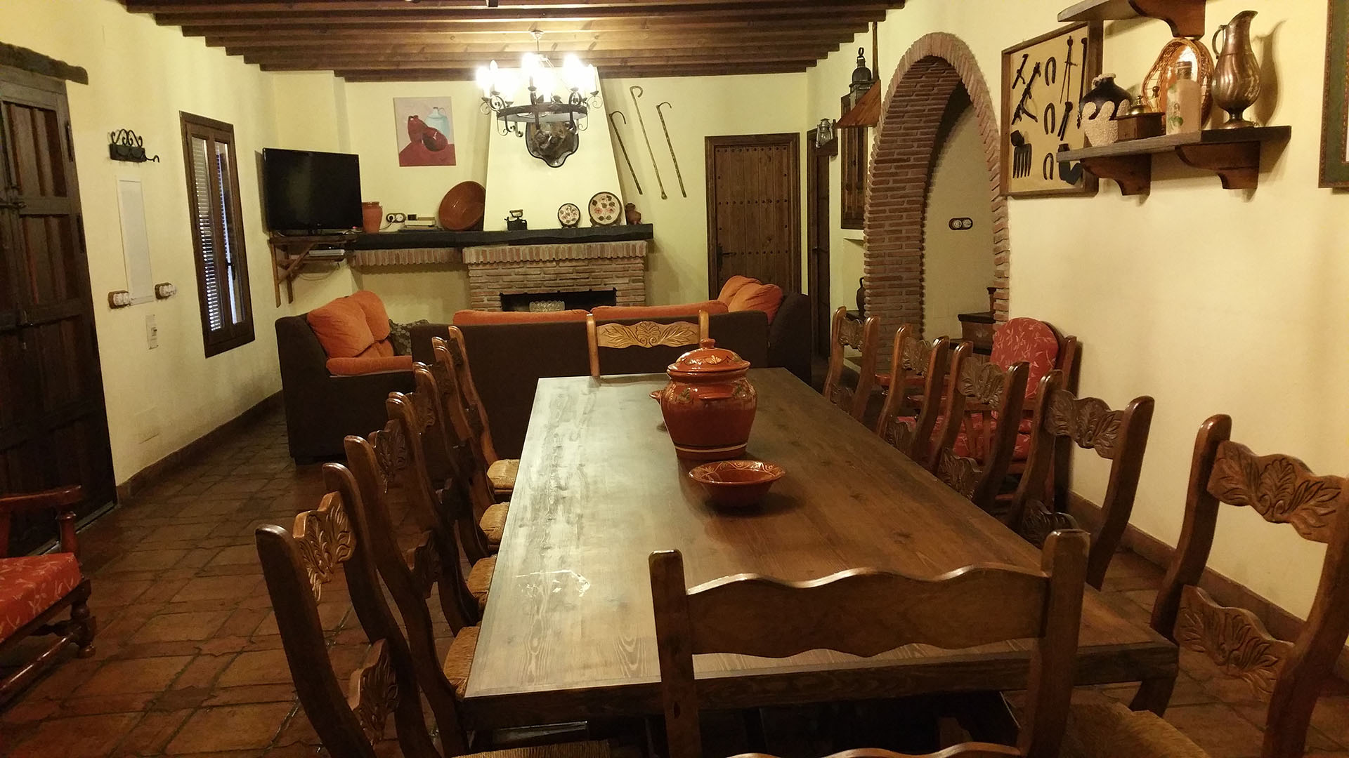 salón con decoración rustica con chimenea al fondo, zona de relax con sofá y mesa de comedor de madera con doce sillas.