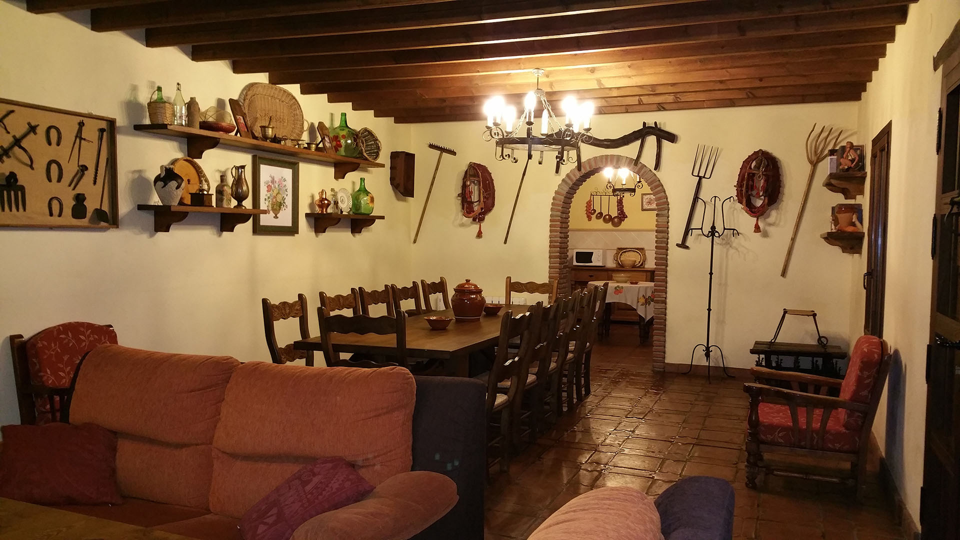 salón con decoración rustica con la cocina al fondo y mesa de comedor de madera con doce sillas.