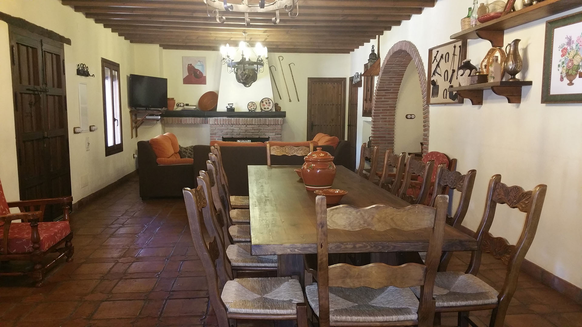 salón con decoración rustica con chimenea al fondo, zona de relax con sofá y mesa de comedor de madera con doce sillas.